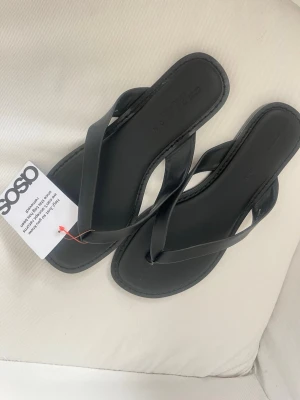 Svarta flip-flops från ASOS - Stilrena svarta flip-flops från ASOS i läderimitation. Aldrig använda, lappen kvar!