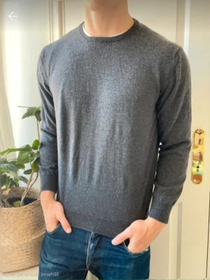 Mörkgrå stickad tröja Gran Sasso - Mörkgrå stickad tröja från Gran Sasso i klassisk modell med rund halsringning och långa ärmar. Tröjan har ribbade muddar vid ärmslut och nederkant. Perfekt för lager på lager och enkel att matcha till olika outfits.