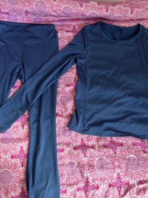 Mörkblått träningsset - Säljer ett mörkblått träningsset med långärmad tröja och matchande tights. Setet är tillverkat i ett stretchigt och mjukt material som passar perfekt för gym, yoga eller löpning. Tröjan har rund halsringning och tightsen har hög midja för extra komfort.