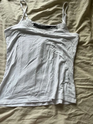 Vit spetsdetaljerad linnetopp - Säljer en vit linnetopp med tunna axelband och fina spetsdetaljer vid urringningen. Perfekt att styla till jeans eller kjol för en fräsch look. Toppen är enkel men ändå söt tack vare spetsen. Använd typ 2 gånger och i väldigt bra skick.