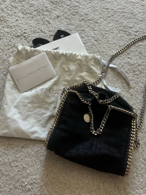 Stella McCartney väska  - Svart Stella McCartney vaska med guldkedjor. Bra skick. Guldfärgen har lossnat lite från kedjan och tyget inuti är lite smutsigt, men inget man tänker på. Modellen är Tiny fallabella. Hör av er om ni vill ha fler bilder💞