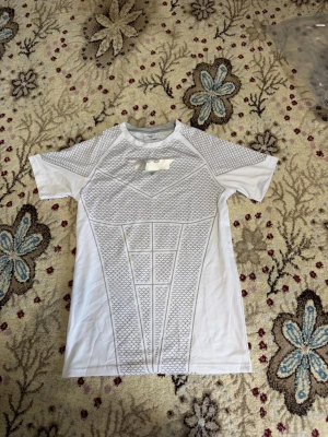 Vit träningströja från YoungLa - Snygg vit t-shirt från YoungLA med Batman-inspirerat tryck och geometriskt mönster. Perfekt för gym och träning. Materialet är stretchigt och andas, med korta ärmar och rund hals. Trycket på bröstet föreställer Batmans logga.