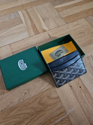 Svart Cardholder lyx - Snyggt svart kortfodral med det klassiska mönstret i vitt och grått. Fodralet har flera fack för kort och levereras i grön ask med gul putsduk. Perfekt för dig som vill ha stilren och exklusiv accessoar.