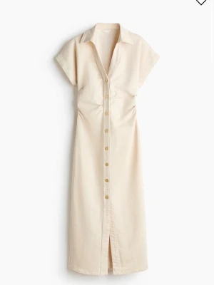 Beige skjortklänning med knappar - Stilren beige skjortklänning med korta ärmar, krage och knappar längs hela framsidan. Klänningen har slits framtill för extra rörelsefrihet. Perfekt för en avslappnad men ändå chic look.