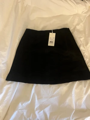 Svart kortkjol i strukturtyg - Säljer en svart kortkjol i strukturtyg med enkel och stilren design. Kjolen har en rak passform och är perfekt att matcha med olika toppar för en trendig look. Passar dig som gillar minimalistisk stil. Ny med prislapp kvar! Aldrig använd! Nypris: 499kr