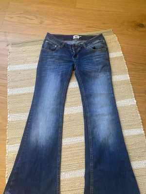 Blå bootcut jeans från lager 157 - Snygga blå bootcut jeans från lager 157 med klassisk femficksdesign och slitningar framtill. Jeansen har låg midja och utsvängda ben, perfekta för en retroinspirerad look. Tillverkade i denim med skön stretch för extra komfort. Short modell!!
