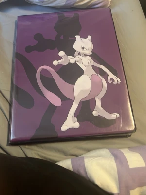 Pokémon samlarpärm med kort - Säljer en lila Pokémon-pärm med Mewtwo på framsidan. Pärmen innehåller flera Pokémonkort i plastfickor, perfekt för dig som vill organisera eller utöka din samling. Omslaget är i plast och motivet är tydligt och färgstarkt.