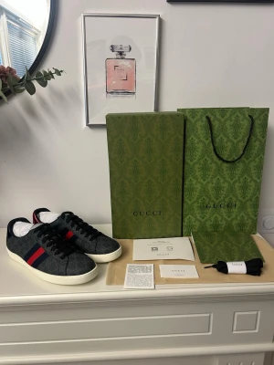 Gucci GG Supreme sneakers svart/blå - Snygga Gucci sneakers i svart GG Supreme canvas med mörkblå och röda ränder på sidan. Skorna har svarta skosnören, vit sula och klassisk låg silhuett. Perfekta för dig som vill ha en exklusiv och trendig look.