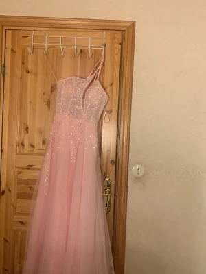 Lång rosa glittrig klänning med snörning - Säljer en lång rosa klänning med tunna axelband och snörning i ryggen. Klänningen har glittriga detaljer på överdelen och ett flytande, tunt tyg i kjolen. Perfekt för bal eller festliga tillfällen. Den är ny och har används bara 1 gång skriv om ni verkar intresserade ❤️