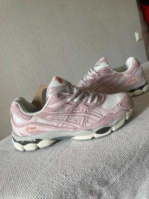 Asics rosa och vita sneakers - Säljer ett par snygga Asics sneakers i ljusrosa och vitt med mesh och mockadetaljer. Skorna har en chunky sula i vitt och grått samt orange Asics-logga på sidan och plösen. Perfekta för dig som gillar sportig och trendig stil.
