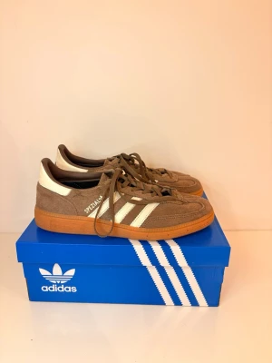 Adidas Spezial bruna sneakers - Adidas Spezial sneakers i mocka med bruna och vita detaljer samt klassiska tre ränder på sidan. Skorna har en låg profil och gummisula i retrostil. Perfekta för dig som gillar streetwear och sportig look. Demhär skorna är används pytte pytte lite !! Perfekta skor och så så sköna ! Passar vilken årstid som helst ! 