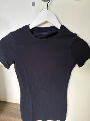 Marinblå t-shirt från Intimissimi - En enkel svart t-shirt från Intimissimi med rund hals och korta ärmar. Modellen är figurnära och tillverkad i mjuk bomull som känns skön mot huden. Perfekt basplagg att matcha med allt i garderoben.