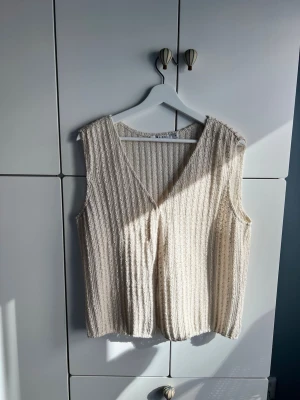 Stickad beige väst från NA-KD - Stickad beige väst från NA-KD i storlek M. Använd 2 gånger och är i fint skick. Hakarna sitter dock lite löst så kan vara bra att sy fast dem lite extra.  Kika gärna på mina andra annonser för bundle.