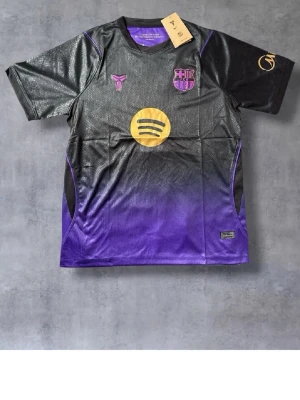 Barcelona Lamine Yamal matchtröja - Snygg Barcelona matchtröja i svart och lila med guldfärgade detaljer. Tröjan har korta ärmar, klubbmärke och Spotify-logga framtill samt Lamine Yamal och nummer 10 på ryggen. Tillverkad i lätt och ventilerande funktionsmaterial, perfekt för fotbollsträning.