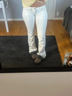 Vita bootcut jeans med låg midja - Säljer ett par vita bootcut jeans med låg midja och klassiska fem fickor. Jeansen har en snygg passform som framhäver benen och är perfekta för dig som gillar en trendig och fräsch look.