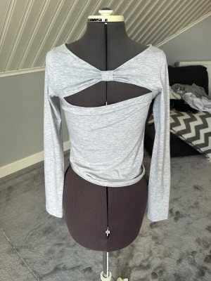Ljusgrå långärmad topp med cut out - Trendig ljusgrå långärmad topp med unik cut out-detalj och twist framtill. Toppen har en tight passform och är tillverkad i mjukt, stretchigt material som känns bekvämt mot huden. Perfekt för dig som vill sticka ut med en cool och modern look.