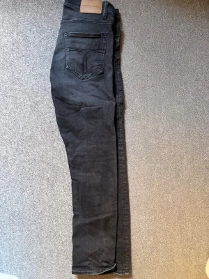 Tiger of Sweden jeans  - Säljer ett par svarta slim fit jeans med klassisk femficksdesign och knappgylf. Jeansen har en snygg tvättad look och raka ben. Perfekta till vardagsstilen och passar till det mesta. Materialet är mjukt och stretchigt för extra komfort.