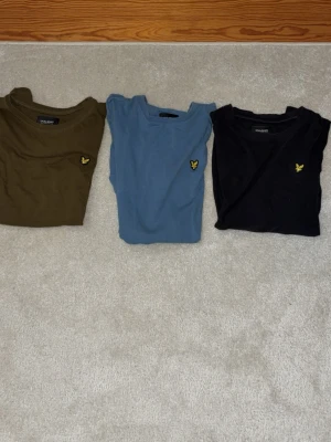 Perfekta T-shirtar – Stilrena, sköna & redo för ny ägare! - En svart t-shirt med rund hals och korta ärmar. På bröstet sitter en liten gul broderad logga som detalj. T-shirten har en klassisk passform och är tillverkad i mjuk bomull, perfekt för en enkel och stilren look.