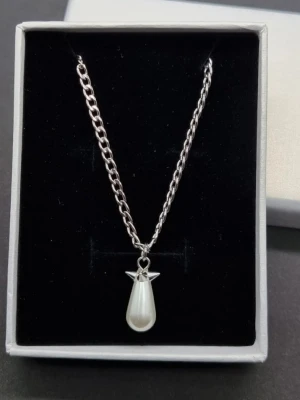 Handgjort halsband inspirerat av Maria Nilsdotter  - Snyggt halsband i silverfärgad metall med en droppformad vit pärla som hänge. Kedjan är medelgrov och ger ett modernt intryck. Perfekt accessoar för att lyfta din outfit med en elegant touch. Längd-50cm
