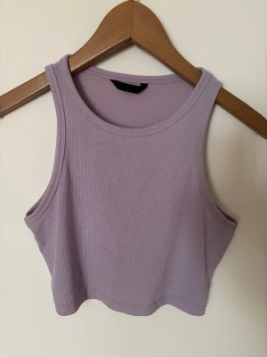 Ljuslila ribbad croppad linnetopp - Säljer en ljuslila croppad linnetopp i ribbad bomull. Toppen är ärmlös med rund halsringning och sitter tight mot kroppen💜