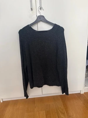 Mörkgrå stickad tröja - En enkel och stilren mörkgrå stickad tröja med rund halsringning och långa ärmar. Tröjan är gjord i ett mjukt, stickat material som passar perfekt till kyligare dagar.