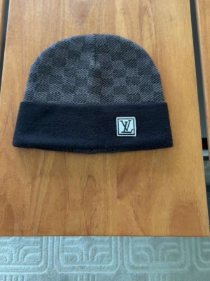 Gråsvart mössa med rutmönster - Snygg gråsvart mössa med diskret rutmönster och vikt kant. På framsidan sitter en patch med LV-loggan. Mössan är i mjukt material och har en klassisk, enkel form som passar till det mesta.