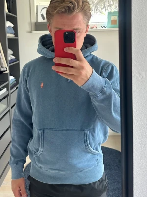 Blå hoodie från Polo Ralph Lauren - Säljer en blå hoodie från Polo Ralph Lauren med en snygg tvättad look. Tröjan har det ikoniska lilla broderade logotypen i orange på bröstet. Mjuk bomullskvalitet och ribbade muddar vid ärmar och nederkant. Storlek s passar även mindre m. 