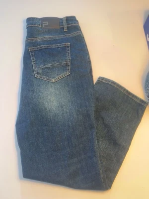 Blå raka jeans med hög midja - Snygga blå jeans med raka ben och hög midja. Jeansen har klassisk femficksdesign, bälteshällor och knappgylf. Materialet är slitstark denim i bomull med lätt tvättade detaljer för en trendig look. 