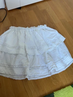 Vit volangkjol - Säljer en fin vit kjol med detaljerade volanger. Den är inte använd mycket så den är gott skick. Köpt på Bikbok och tror att det är storlek XS/S (lappen är inte kvar). Materialet är 100% bomull. Nypris är 399kr, skriv för mått