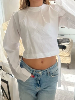 Vit croppad långärmad topp från Zara - Säljer denna super söta vit croppad blus med långa ärmar från Zara. Den är aldrig använd med lappen kvar. Köpte den för 400kr förra året och säljer för 200kr. Den är i storlek xs men den är ganska oversized så skulle säga att den passar alla mellan xs-m. Den går även att justera med bandet där bak. 💞🌸