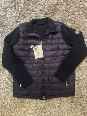Mörkblå Moncler cardigan - Snygg mörkblå cardiganjacka från Moncler med quiltad front och stickade ärmar samt rygg. Tröjan är helt ny i storlek M. 
