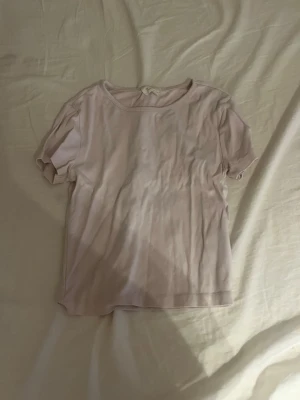 Ljusrosa basic t-shirt - En enkel ljusrosa t-shirt med rund halsringning och korta ärmar. T-shirten har en rak passform och är tillverkad i ett mjukt, tunt material som känns skönt mot huden. Perfekt att matcha med jeans eller kjol för en avslappnad look. Och den är ganska kort