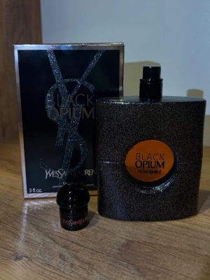 Yves Saint Laurent Black Opium parfym - Black Opium, de är en ikonisk parfym i en svart, glittrig flaska med rund orange etikett. Flaskan har en modern, fyrkantig form och medföljande originalkartong. Doften är känd för sin djupa, sensuella karaktär och passar perfekt för dig som vill sticka ut.