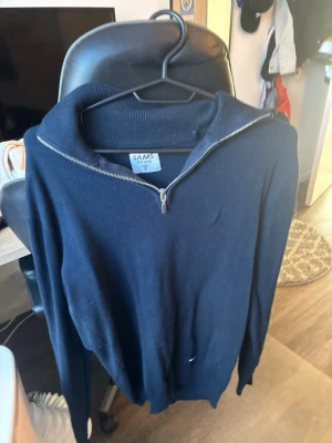 Mörkblå tröja med dragkedja från SAMS - Mörkblå stickad tröja från SAMS med halv dragkedja vid kragen. Tröjan har ribbstickad krage och muddar, perfekt för lager-på-lager. Enkel och stilren design som funkar till många outfits.