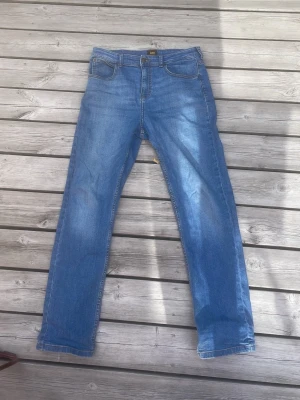 Blå raka jeans från Lee - Storlek 15-16 y. Snygga blå jeans från Lee med rak passform och klassisk femficksdesign. Jeansen har normal midja och är tillverkade i ett slitstarkt denimtyg. Perfekta för en avslappnad och trendig look.