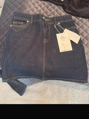 Mörkblå jeanskjol från ONLY - Trendig mörkblå jeanskjol från ONLY i klassisk femficksmodell. Kjolen har kontrastsömmar, knapp- och dragkedjestängning samt kort, rak passform. Perfekt att matcha med sneakers eller boots för en cool look.