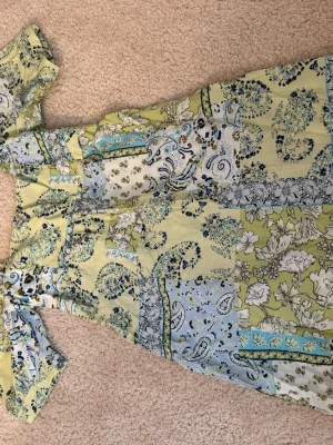 Blommig kortklänning i pastell - Söt kortklänning med blommigt och paisleymönster i ljusgult, blått och grönt. Klänningen har puffiga korta ärmar, smockad rygg och fyrkantig urringning. (Aldrig använd)