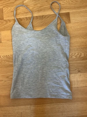 Grå linnetopp från Gina Tricot - Säljer en enkel och stilren grå linnetopp från Gina Tricot. Toppen har tunna axelband och är tillverkad i mjuk bomullsmix, perfekt för lager på lager eller till varma dagar.