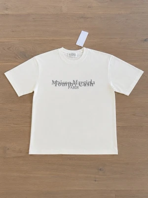 Vit Maison Margiela t-shirt - Säljer en vit t-shirt från Maison Margiela med tryck framtill och siffror på ryggen. T-shirten har klassisk passform, rund hals och korta ärmar. Perfekt för dig som gillar minimalistisk och stilren design.