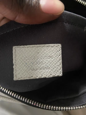 Vit handväska från Louis Vuitton - Snygg vit handväska från Louis Vuitton med klassiskt monogrammönster. Väskan är tillverkad i strukturerat läder och har silverfärgad dragkedja. Perfekt accessoar för dig som gillar exklusiv och tidlös design.