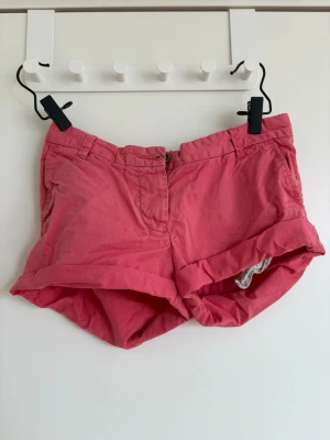 Rosa shorts från Maison Scotch - Säljer ett par snygga rosa shorts från Maison Scotch. De har uppvikta benslut, bälteshällor och dragkedja framtill. Perfekta för varma dagar och har en avslappnad passform. Klassisk design som funkar till det mesta.