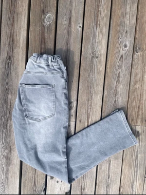 Ljusgrå raka jeans med resårmidja - Säljer ett par ljusgrå jeans med raka ben och resår i midjan. Jeansen har två bakfickor och klassisk denimlook. Perfekta för en avslappnad och trendig stil. Materialet känns mjukt och bekvämt, passar till många olika outfits.