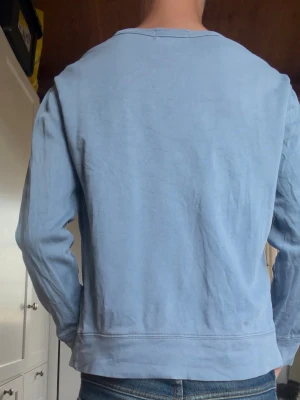 Ljusblå sweatshirt från Polo Ralph Lauren - Ljusblå sweatshirt med rund hals och långa ärmar från Polo Ralph Lauren. Tröjan har en liten broderad logga på bröstet och ribbade muddar vid ärmslut och nederkant. Perfekt för en avslappnad och stilren look.