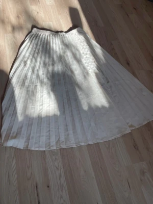 Ljusbeige plisserad långkjol - Säljer en superfin ljusbeige långkjol med plisserade veck och elastisk midja. Kjolen har ett skirt, glansigt material som ger ett elegant intryck och passar perfekt till olika stilar. Perfekt för dig som gillar en flowy och trendig look.