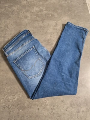 Ljusblå jeans från Jack & Jones - Säljer ett par ljusblå jeans från Jack & Jones med klassisk femficksdesign och raka ben. Jeansen har en snygg tvättad look och är tillverkade i mjukt denimtyg. Perfekta för en avslappnad stil.