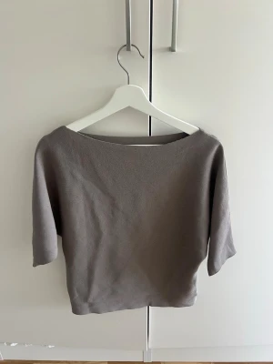 Elegant beige topp med trekvartsärm - En enkel och stilren beige topp med trekvartsärm och bred halsringning. Toppen är tillverkad i ett mjukt material som känns skönt mot huden. Perfekt att matcha med jeans eller kjol för en avslappnad look.