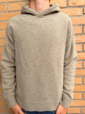 Beige stickad hoodie med huva - Tjena! säljer nu en beige stickad hoodie i mjukt material. Hoodien har en enkel och clean design utan tryck eller detaljer, med ribbade muddar vid ärmar och nederkant. Riktigt fin tröja som man enkelt kan styla svin bra! Andvänd ett fåtal gånger. 