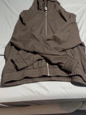 Brunt loungewear-set med hoodie - Mysigt loungewear-set i mjukt brunt tyg. Setet består av en hoodie med dragkedja, huva och ribbade muddar samt ett par vida byxor med avslappnad passform. Perfekt för chill dagar hemma eller när du vill vara bekväm.