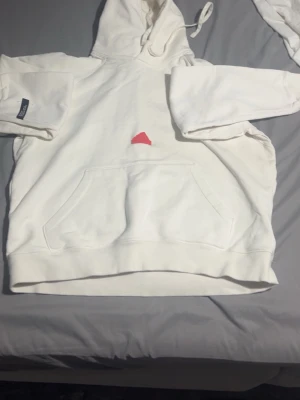 Vit hoodie från Adidas med logga - Säljer en vit hoodie från Adidas med huva och känguruficka. Hoodien har en diskret svart Adidas-logga på bröstet och är tillverkad i mjukt material. Perfekt för en chill och sportig stil.