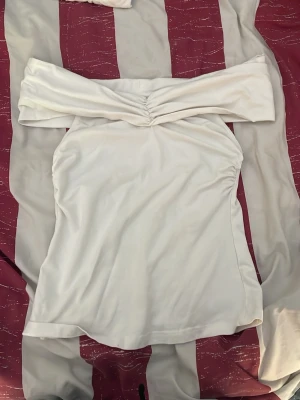 Vit offshoulder kortklänning - Säljer en snygg vit tröja med offshoulder-design och rynkdetalj framtill. Tröjan har en figurnära passform och är tillverkad i ett mjukt, stretchigt material som ger en bekväm känsla. Perfekt för dig som vill ha en stilren och trendig look.
